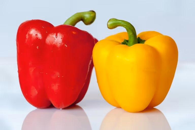 Colorful red and yellow bell peppers on a dark surface, representing the nutritious vegetable base for a healthy sausage and peppers recipe