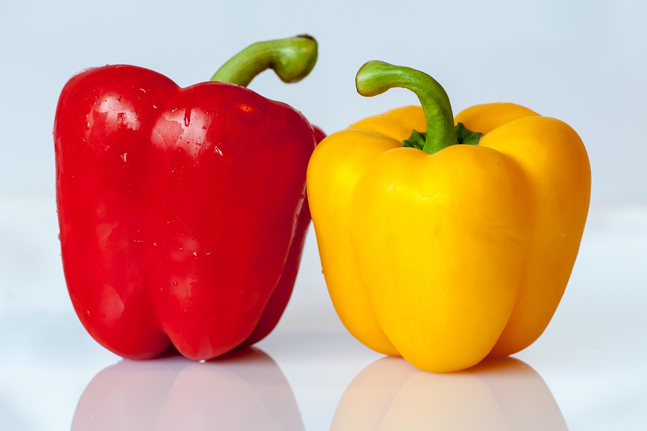 Colorful red and yellow bell peppers on a dark surface, representing the nutritious vegetable base for a healthy sausage and peppers recipe