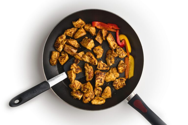 Golden brown chicken thighs and Italian sausage cooking in a skillet with garlic and cherry peppers for chicken scarpariello, a protein-packed one-pan Italian American dinner