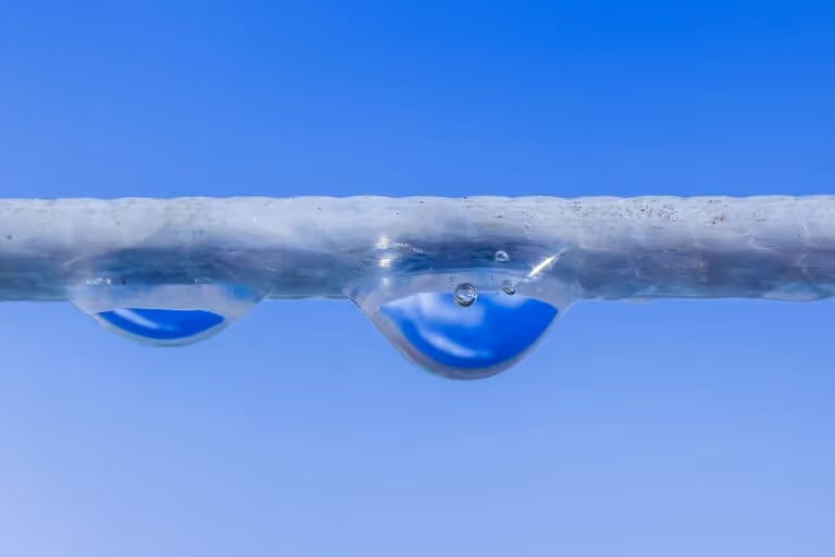 Close-up of a water droplet with air bubbles inside against a soft blue sky background, representing water purification and nanobubble technology for removing microplastics from water.