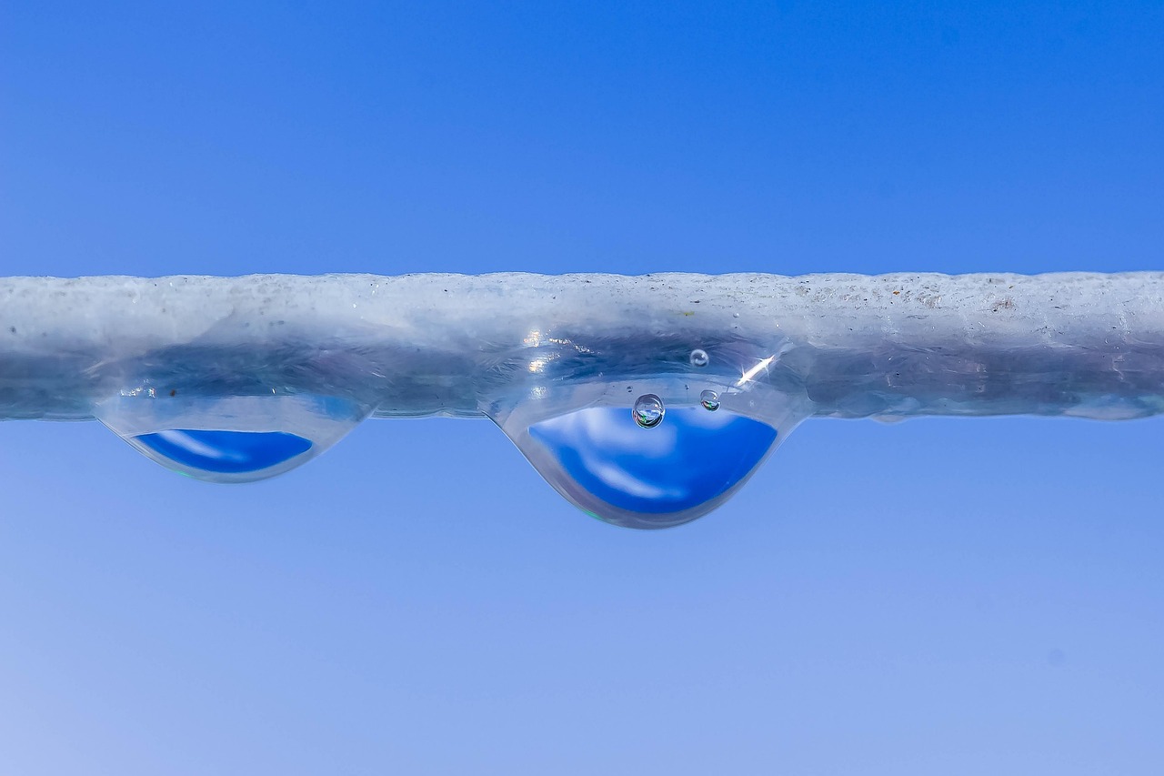 Close-up of a water droplet with air bubbles inside against a soft blue sky background, representing water purification and nanobubble technology for removing microplastics from water.