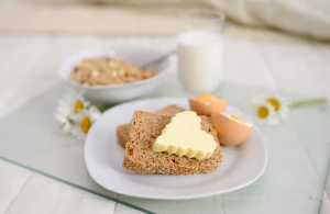 A balanced breakfast spread featuring cereal with milk, fresh bread with butter, and boiled eggs on a tray in bed - showcasing energizing breakfast foods for sustained morning energy