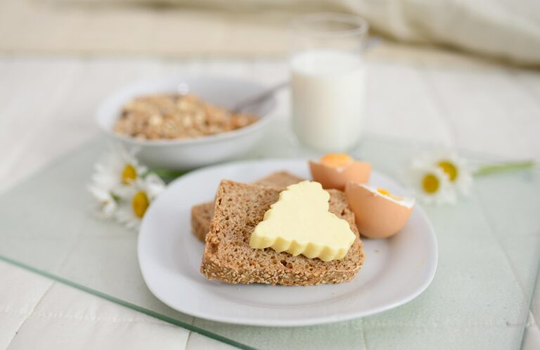 A balanced breakfast spread featuring cereal with milk, fresh bread with butter, and boiled eggs on a tray in bed - showcasing energizing breakfast foods for sustained morning energy