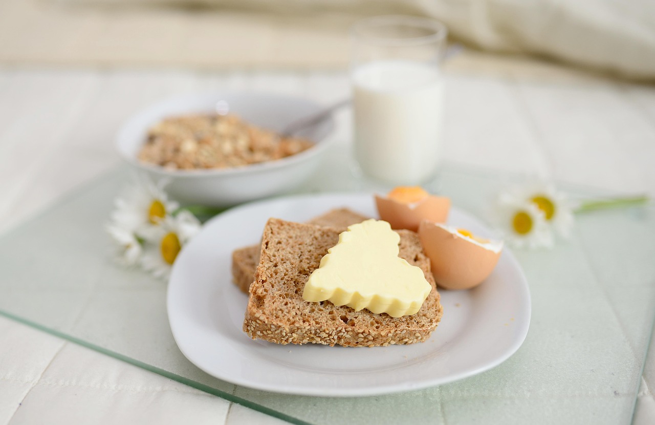 A balanced breakfast spread featuring cereal with milk, fresh bread with butter, and boiled eggs on a tray in bed - showcasing energizing breakfast foods for sustained morning energy