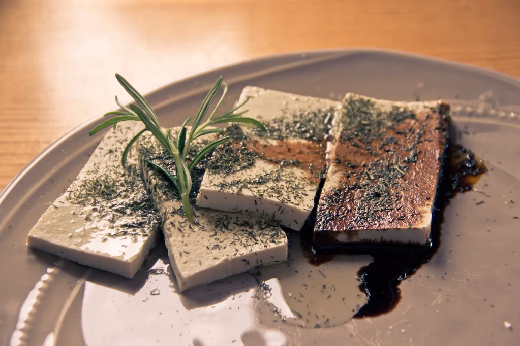 A block of fresh tofu on a plate with green leafy vegetables, representing a whole food plant-based protein option with minimal processing