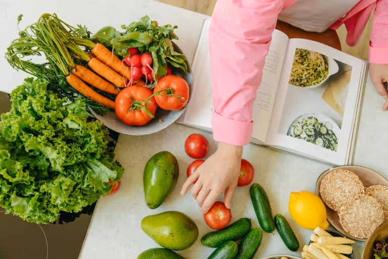 Fresh colorful vegetables and a cookbook on a wooden table, representing anti-inflammatory ingredients for healthy meal prep recipes