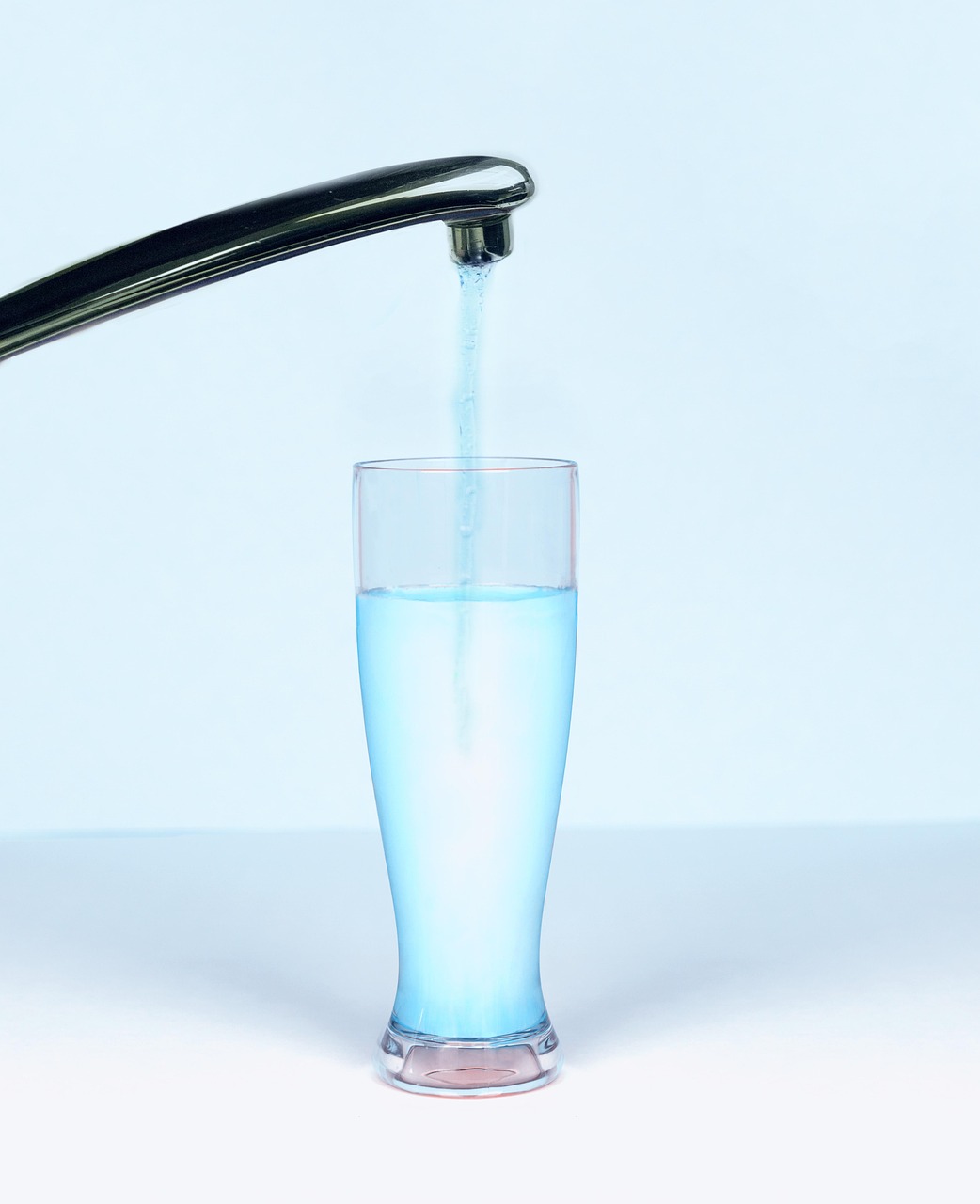 Clear drinking water being poured from a faucet into a glass, representing tap water quality and nanoplastics concerns