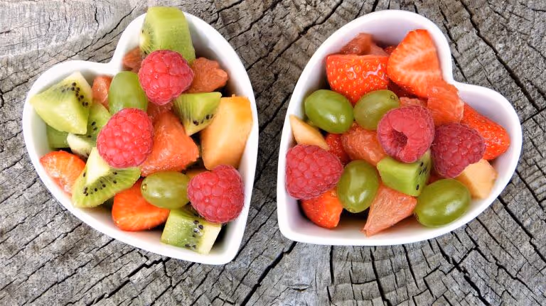 Assorted fresh fruits including berries, bananas, and oranges arranged in heart-shaped bowls on a table, representing heart healthy fruits for cardiovascular wellness