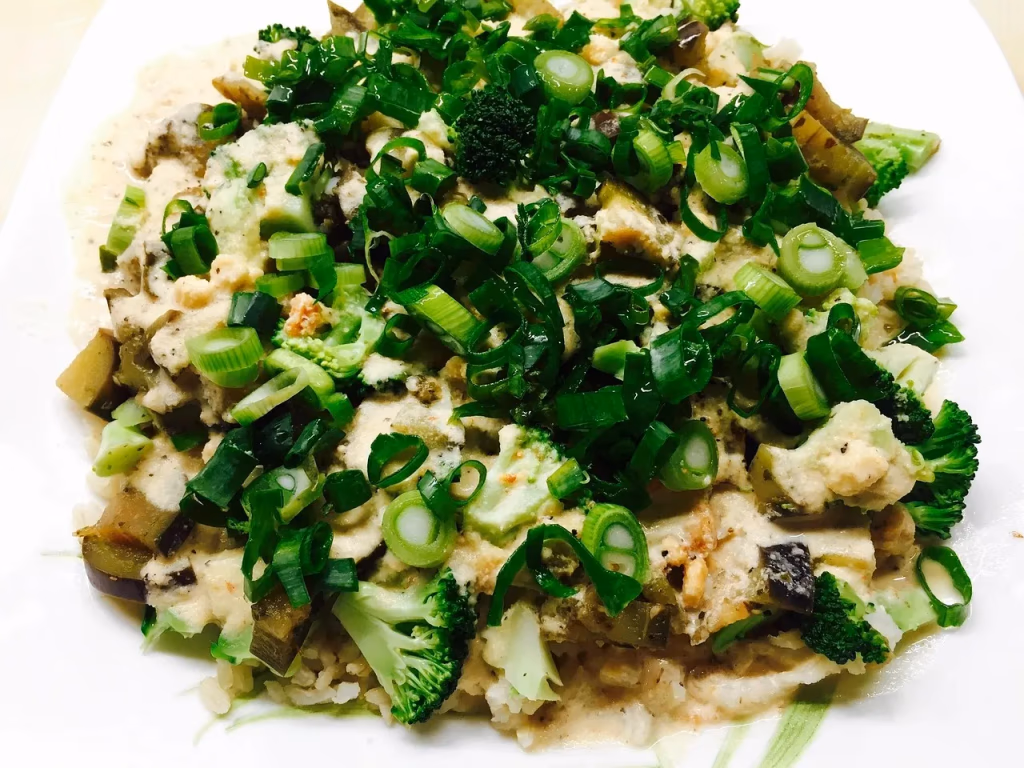 A colorful, healthy plate of cooked vegetables including broccoli, eggplant, and green onions with brown rice and sauce, representing a Mediterranean-style plant-based low protein diet for longevity