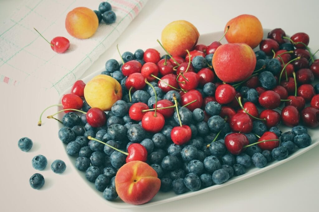 Fresh cherries, blueberries, apricots and other summer fruits arranged on a rustic kitchen surface, representing healthy cherry recipes for sleep, exercise recovery, heart health and blood sugar balance