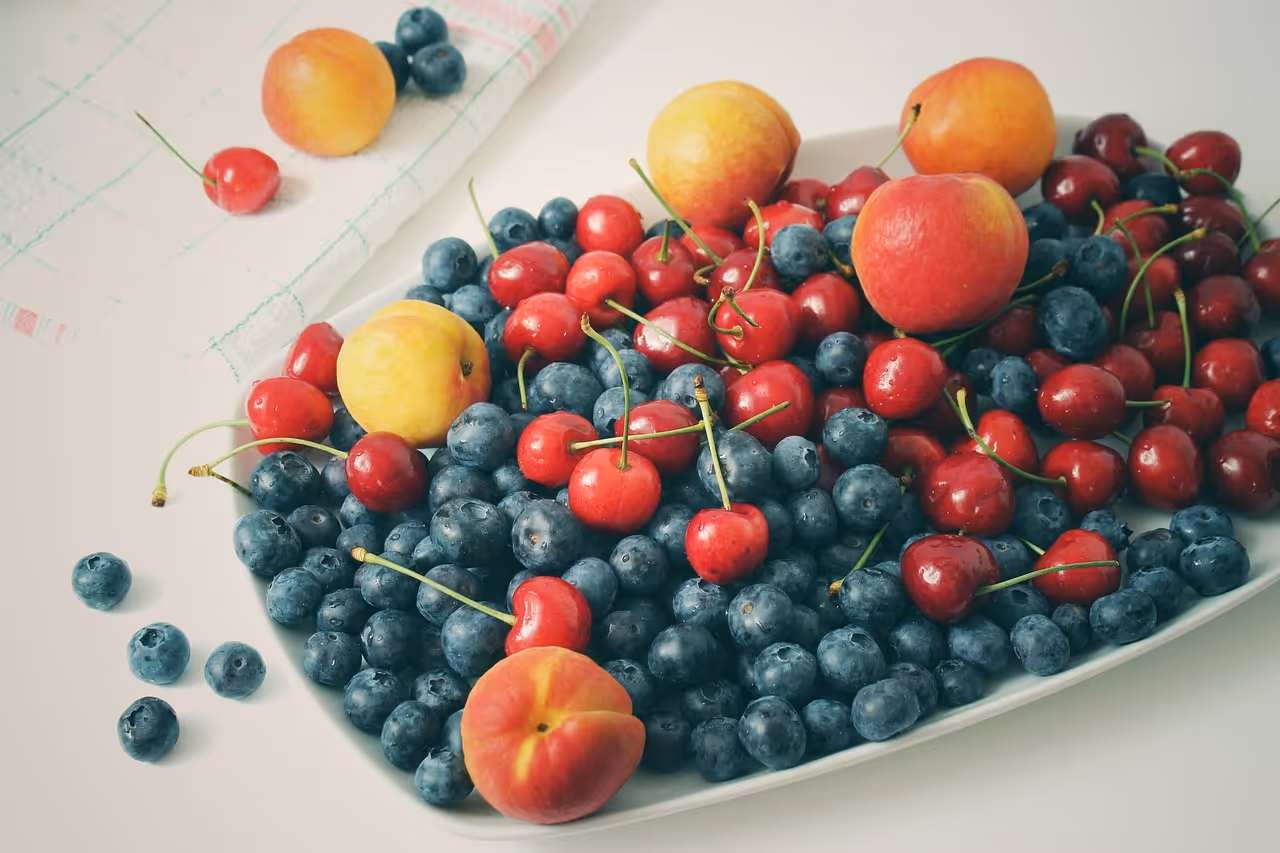 Fresh cherries, blueberries, apricots and other summer fruits arranged on a rustic kitchen surface, representing healthy cherry recipes for sleep, exercise recovery, heart health and blood sugar balance
