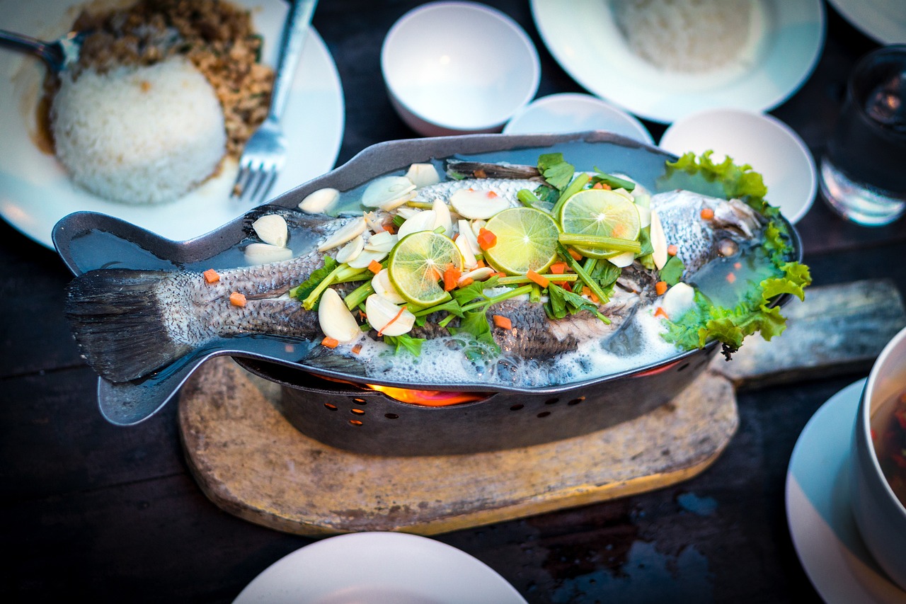 A beautifully plated whole steamed fish with fresh herbs, lime slices, and vegetables, representing a healthy high-protein dinner perfect for summer meal planning.