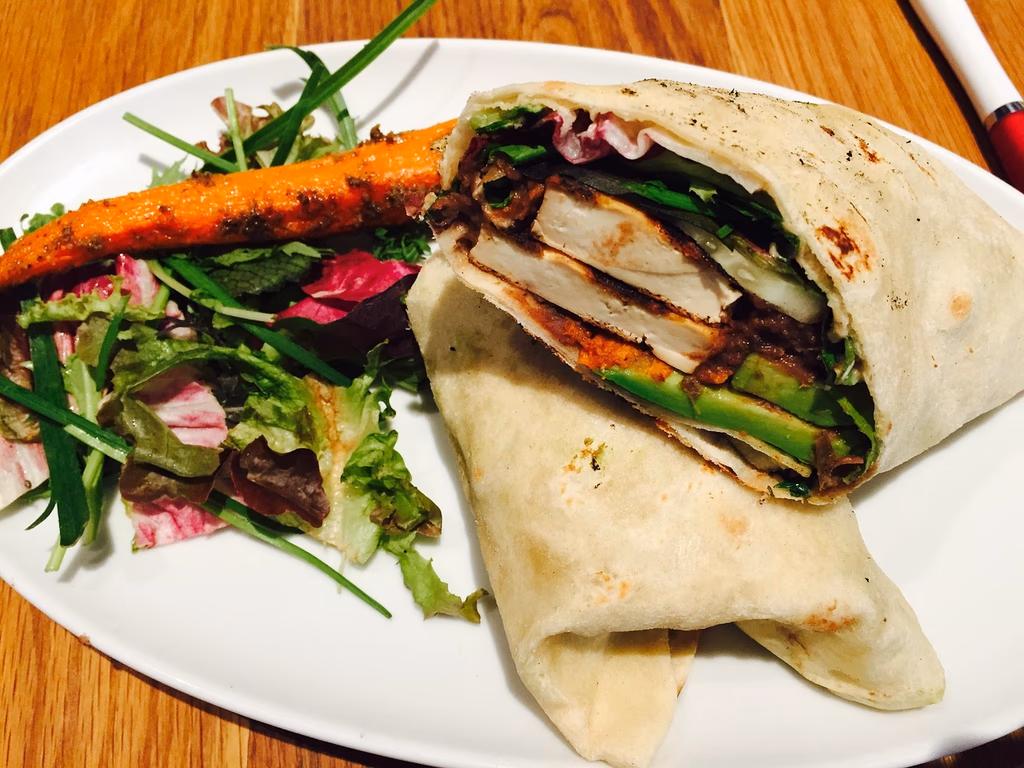 A healthy wrap filled with chicken, avocado, and vegetables, served with a side salad and roasted carrots, representing a balanced high-protein high-fiber meal for better blood sugar management