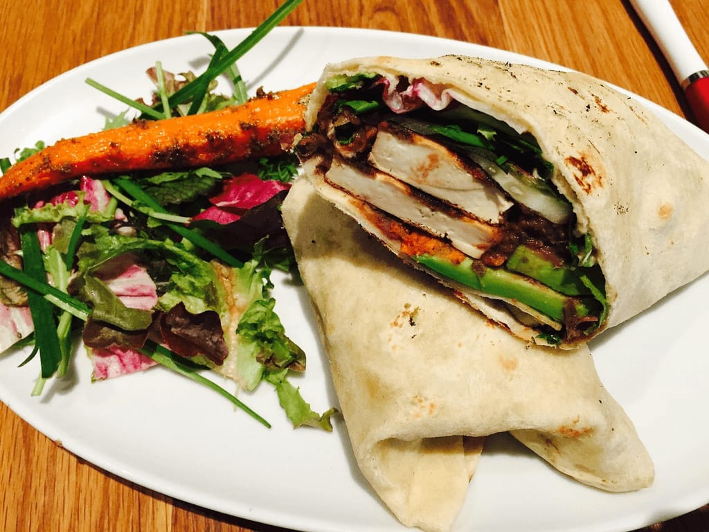 A healthy wrap filled with chicken, avocado, and vegetables, served with a side salad and roasted carrots, representing a balanced high-protein high-fiber meal for better blood sugar management