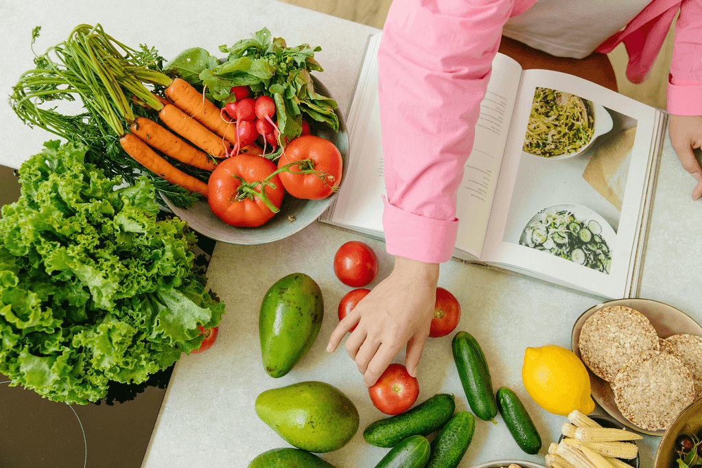 Fresh vegetables including tomatoes, peppers, and greens arranged with a cookbook, representing healthy anti-inflammatory dinner recipes made with fiber-rich ingredients.