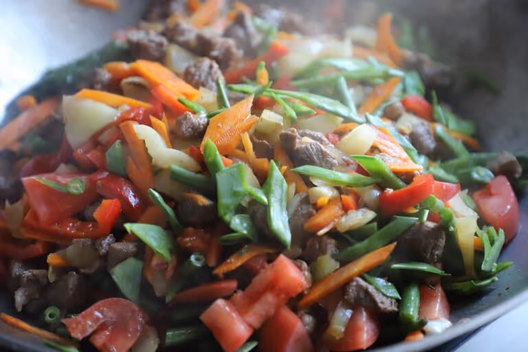 A close-up view of a colorful vegetable and meat stir-fry being cooked in a traditional wok, showing fresh broccoli, peppers, and other vegetables with minimal oil for healthy wok cooking.