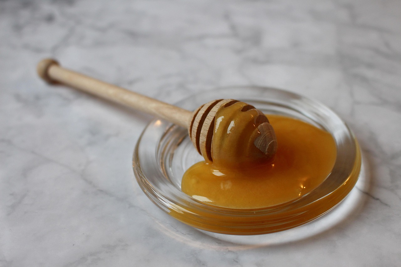 Honey drizzling from a wooden dipper into a small white dish, with a warm golden glow representing natural sweetness and the honey vs sugar health comparison