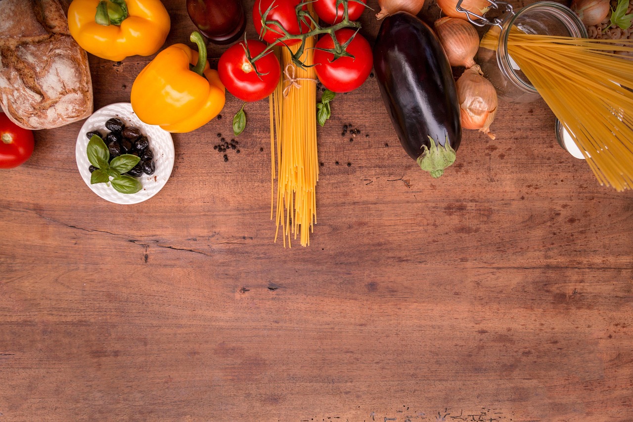Fresh Mediterranean diet ingredients including vegetables, olives, pasta and herbs arranged on a wooden board, representing heart-healthy whole foods rich in healthy fats and nutrients