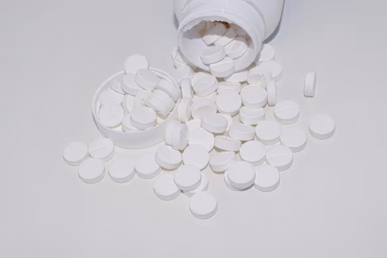 White supplement pills and tablets spilling out of a glass bottle, representing sleep aids like magnesium and melatonin supplements for better sleep quality