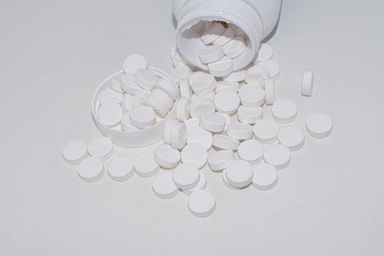 White supplement pills and tablets spilling out of a glass bottle, representing sleep aids like magnesium and melatonin supplements for better sleep quality