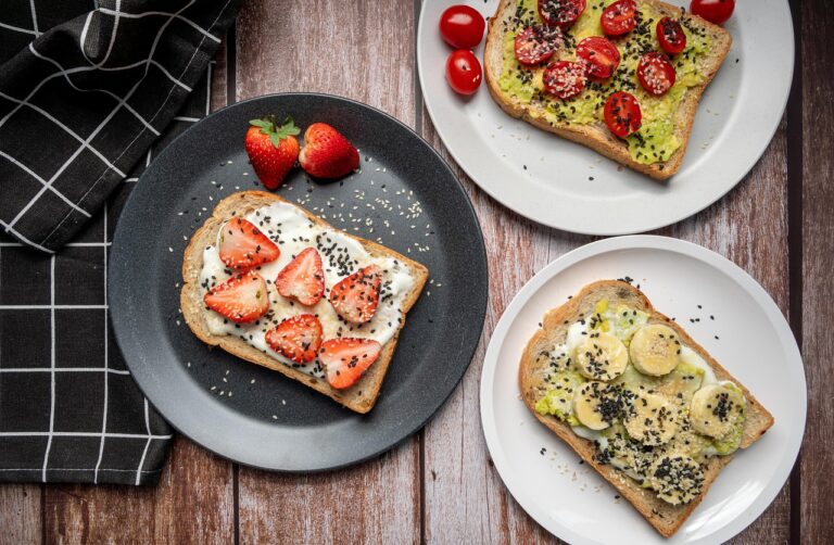 Flat lay of healthy snack pairing ingredients - whole-grain toast topped with avocado, sliced banana, strawberries, and chia seeds on a wooden board