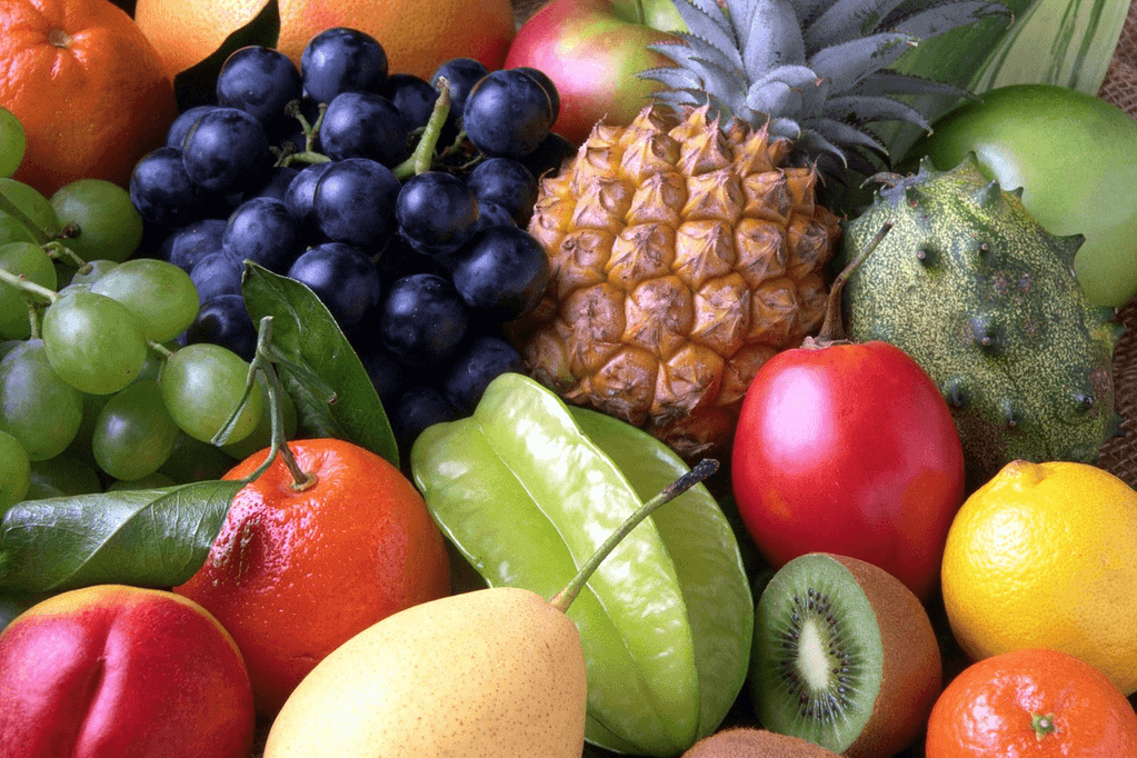A colorful assortment of fresh, peelable fruits including pineapple, oranges, kiwi, lemons, pears and star fruit displayed on a table - safe produce options to eat during the cyclosporiasis outbreak