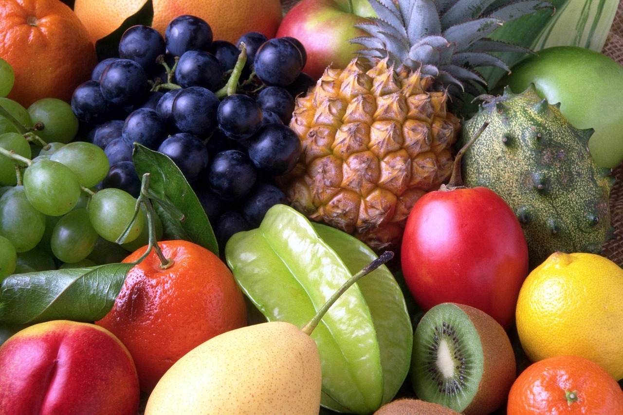 A colorful assortment of fresh, peelable fruits including pineapple, oranges, kiwi, lemons, pears and star fruit displayed on a table - safe produce options to eat during the cyclosporiasis outbreak