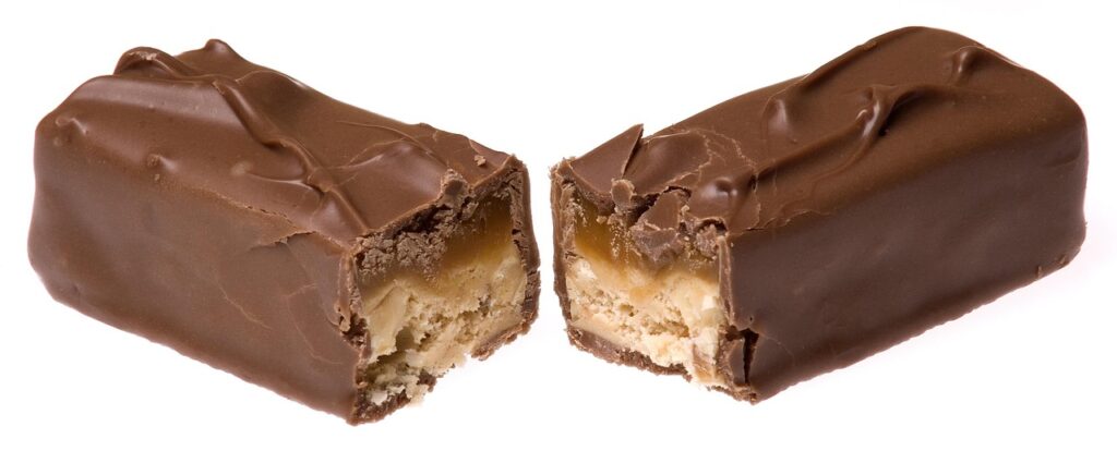 A chocolate bar being broken in half, symbolizing the sweet food cravings that research has linked to early cognitive changes in some forms of dementia. Image represents the article topic of dementia food cravings.