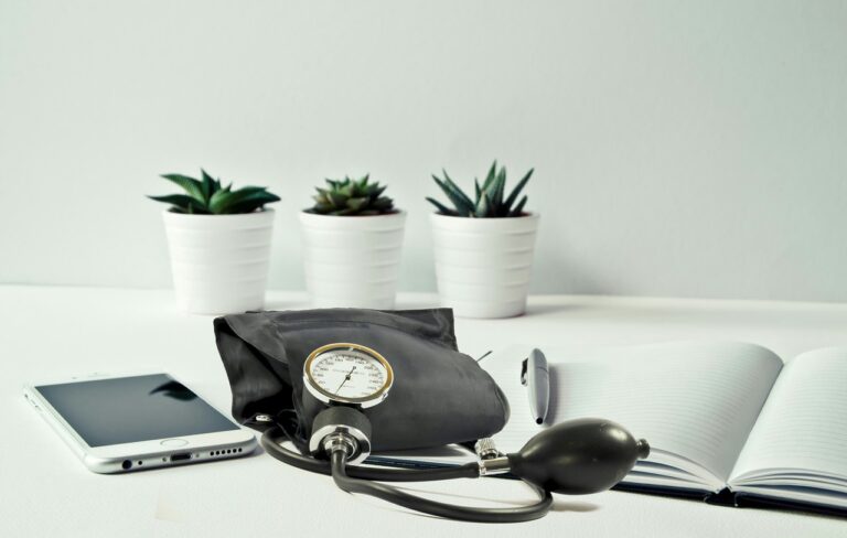 A blood pressure monitor, smartphone, and notebook on a clean desk, representing home blood pressure monitoring and heart health management for women