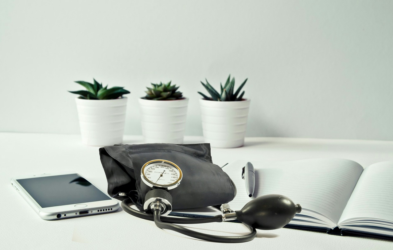 A blood pressure monitor, smartphone, and notebook on a clean desk, representing home blood pressure monitoring and heart health management for women