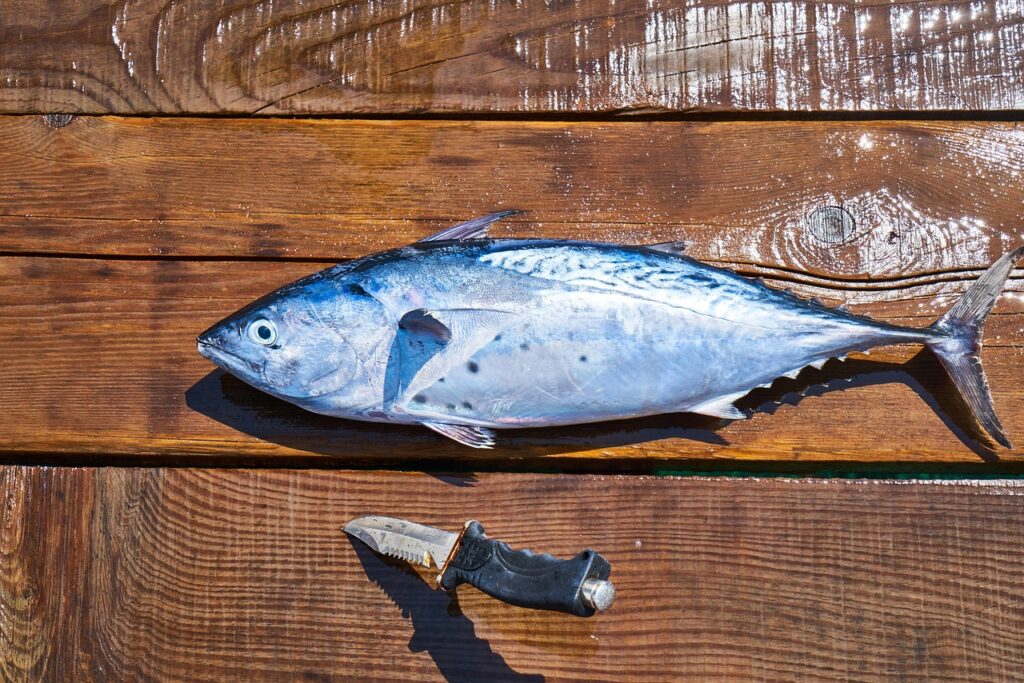 Fresh raw whole fish on a wooden cutting board with herbs, representing omega-3 fatty acid food sources that may help support skin health and reduce psoriasis inflammation