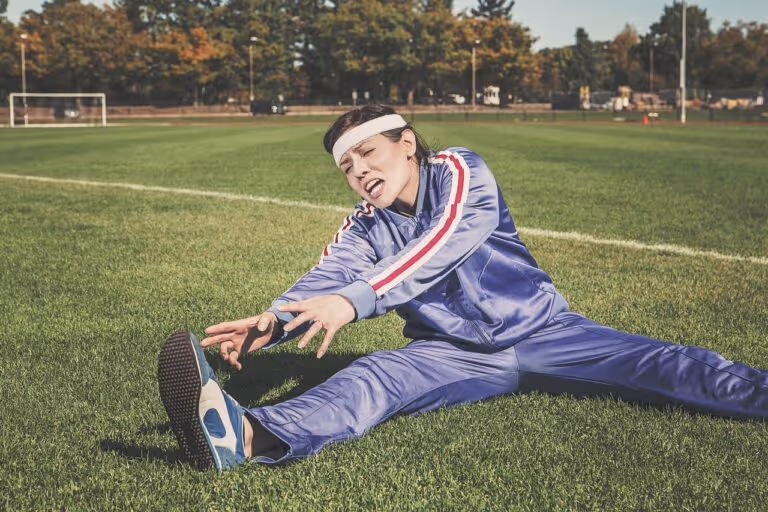 Young woman stretching on a grassy field in athletic wear, representing exercise personality type and finding the right workout for your unique traits