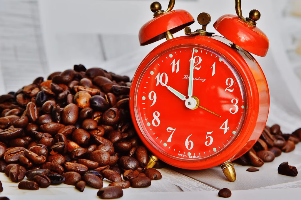 Coffee beans scattered next to an alarm clock on a table, representing the link between morning coffee and liver health benefits
