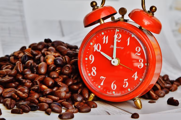 Coffee beans scattered next to an alarm clock on a table, representing the link between morning coffee and liver health benefits
