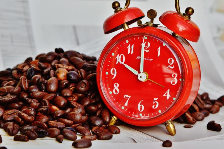 Coffee beans scattered next to an alarm clock on a table, representing the link between morning coffee and liver health benefits
