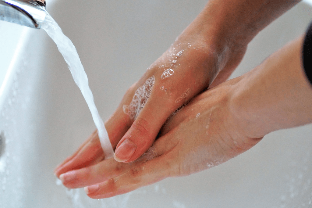 Close-up of hands being washed with soap and water under a faucet, representing hygiene and cyclosporiasis prevention through proper handwashing and food safety practices.