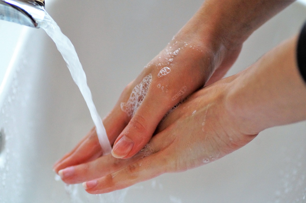 Close-up of hands being washed with soap and water under a faucet, representing hygiene and cyclosporiasis prevention through proper handwashing and food safety practices.
