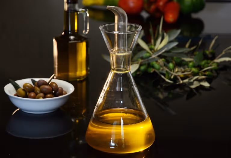 A bottle of extra virgin olive oil surrounded by fresh olives on a wooden surface, representing high-polyphenol olive oil for heart health