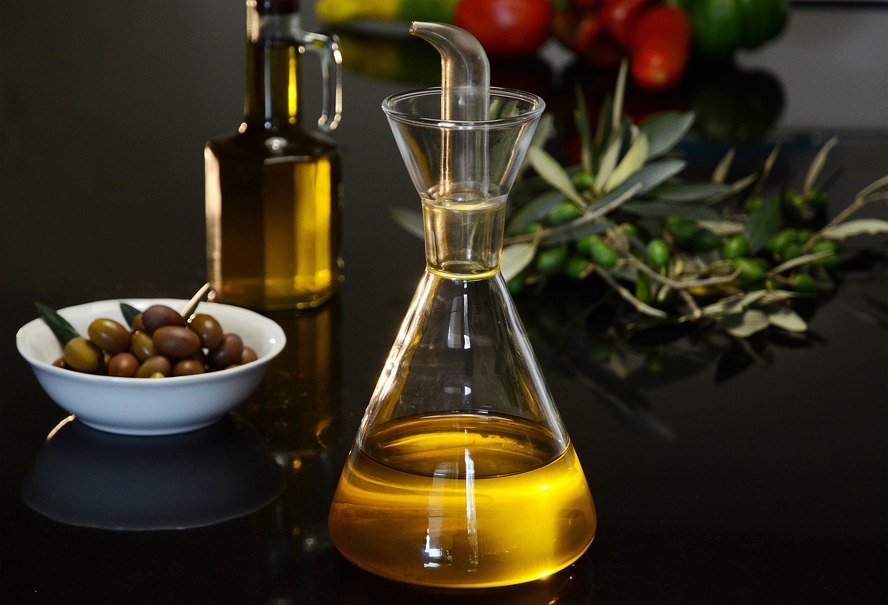 A bottle of extra virgin olive oil surrounded by fresh olives on a wooden surface, representing high-polyphenol olive oil for heart health