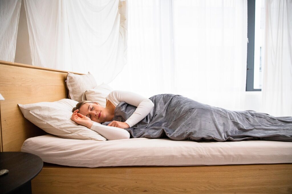 Woman sleeping peacefully on a non-toxic organic mattress in a bright, natural bedroom with wood tones, representing healthy sleep and wellness