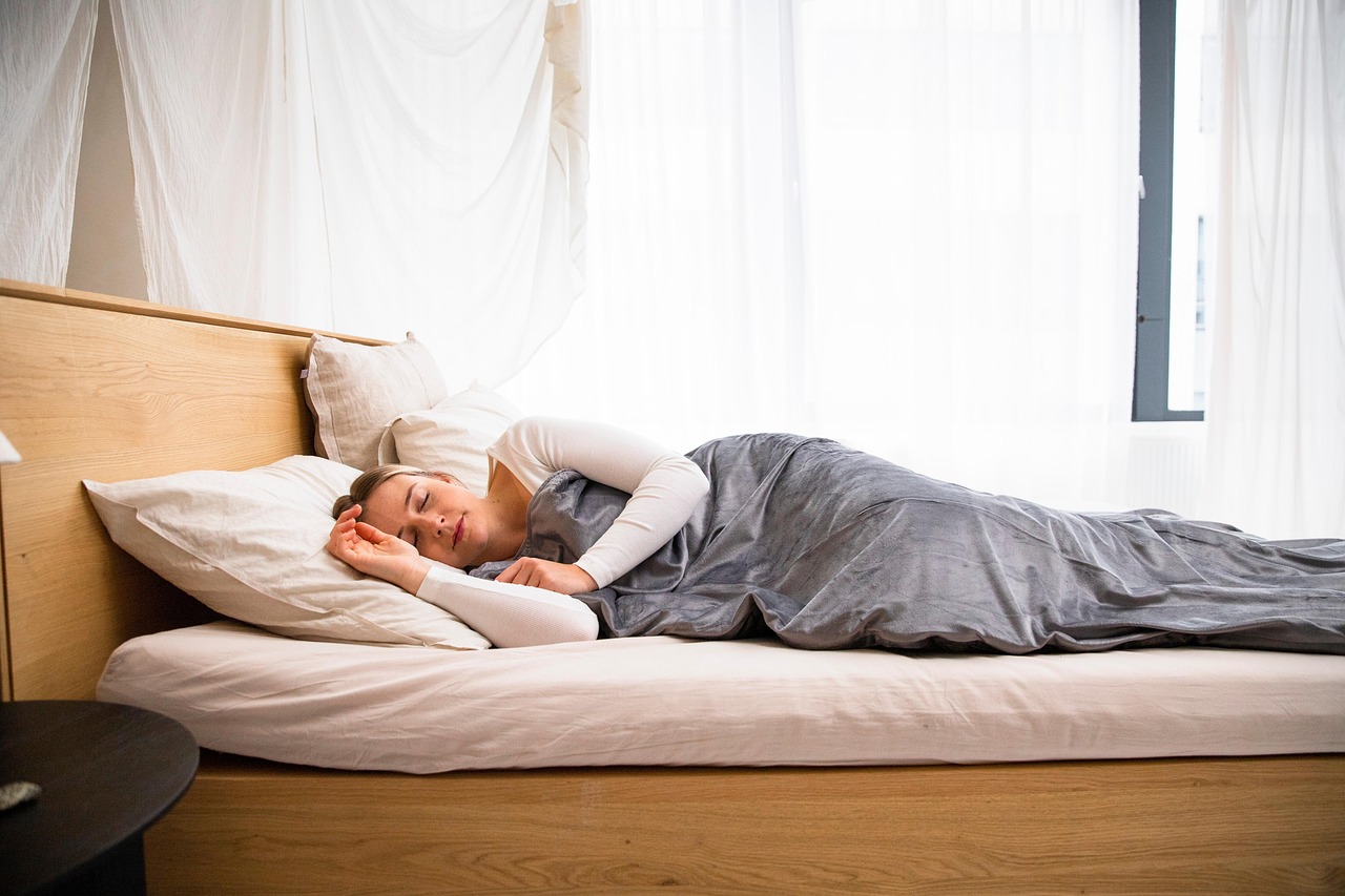 Woman sleeping peacefully on a non-toxic organic mattress in a bright, natural bedroom with wood tones, representing healthy sleep and wellness