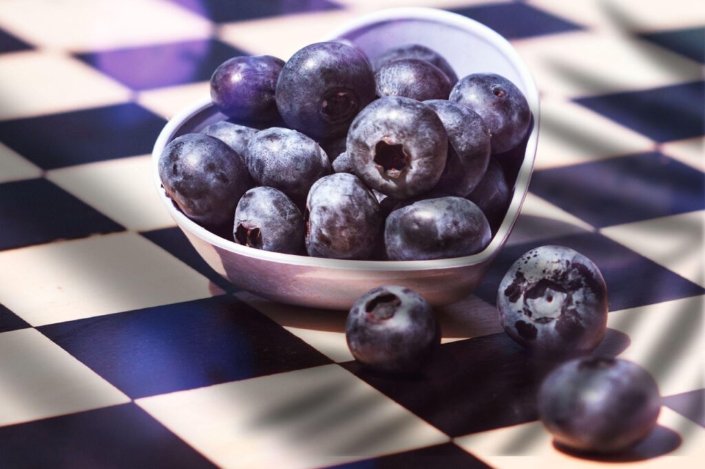Blueberries in a heart-shaped ceramic bowl on a black and white checkered tablecloth, representing a heart healthy breakfast with antioxidant-rich fruit