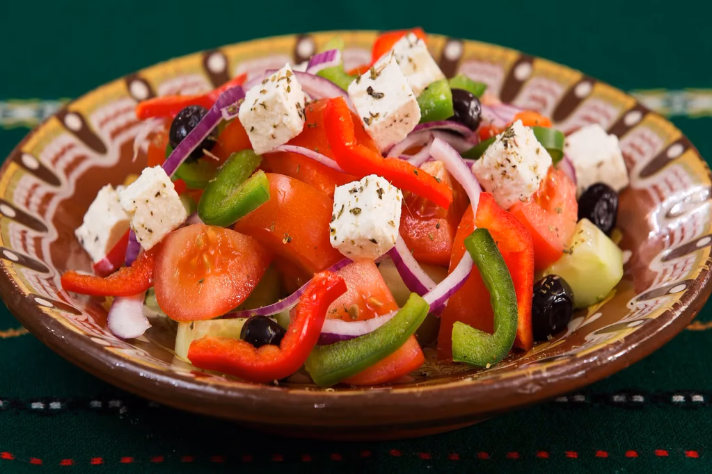 Fresh Mediterranean Greek salad with feta cheese, tomatoes, cucumbers, olives, and peppers on a wooden table - perfect pairing for feta brined chicken bowls