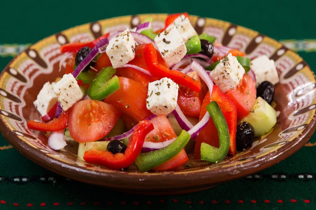 Fresh Mediterranean Greek salad with feta cheese, tomatoes, cucumbers, olives, and peppers on a wooden table - perfect pairing for feta brined chicken bowls