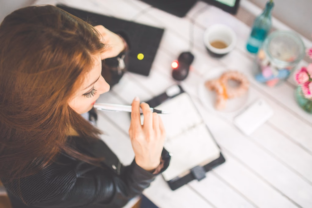 A woman sitting at her desk in an office, looking thoughtful and contemplative while working on a laptop, representing early dementia signs that can show up as subtle changes in workplace performance years before diagnosis.