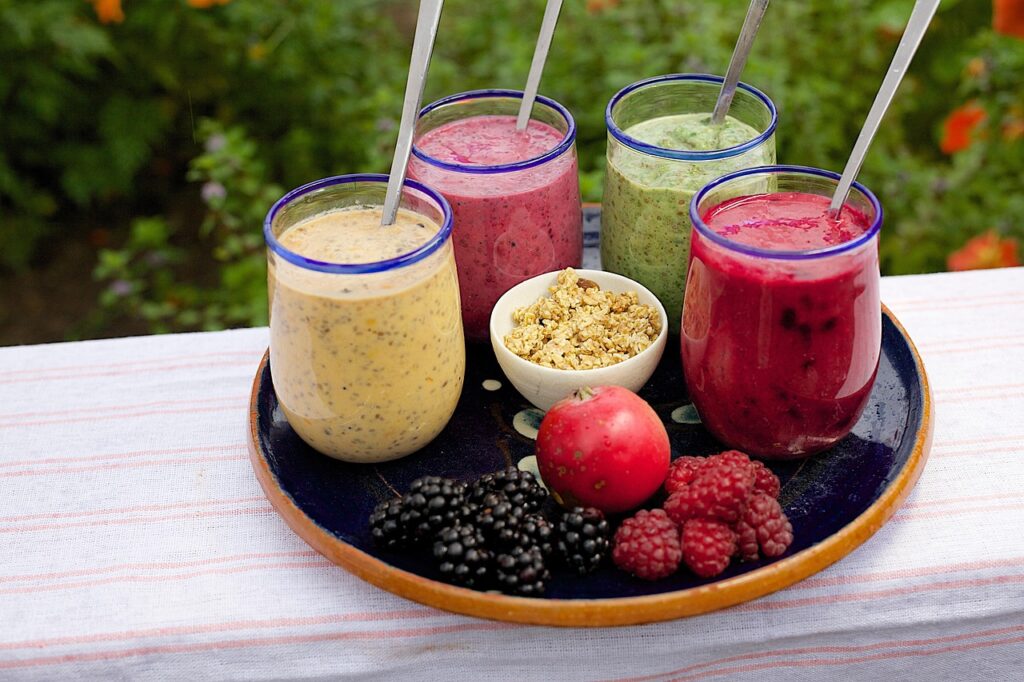 Colorful smoothies in glasses on a table, with fresh blueberries, raspberries, and granola nearby — perfect for a high fiber smoothie breakfast with banana, blueberry, and chia seeds.