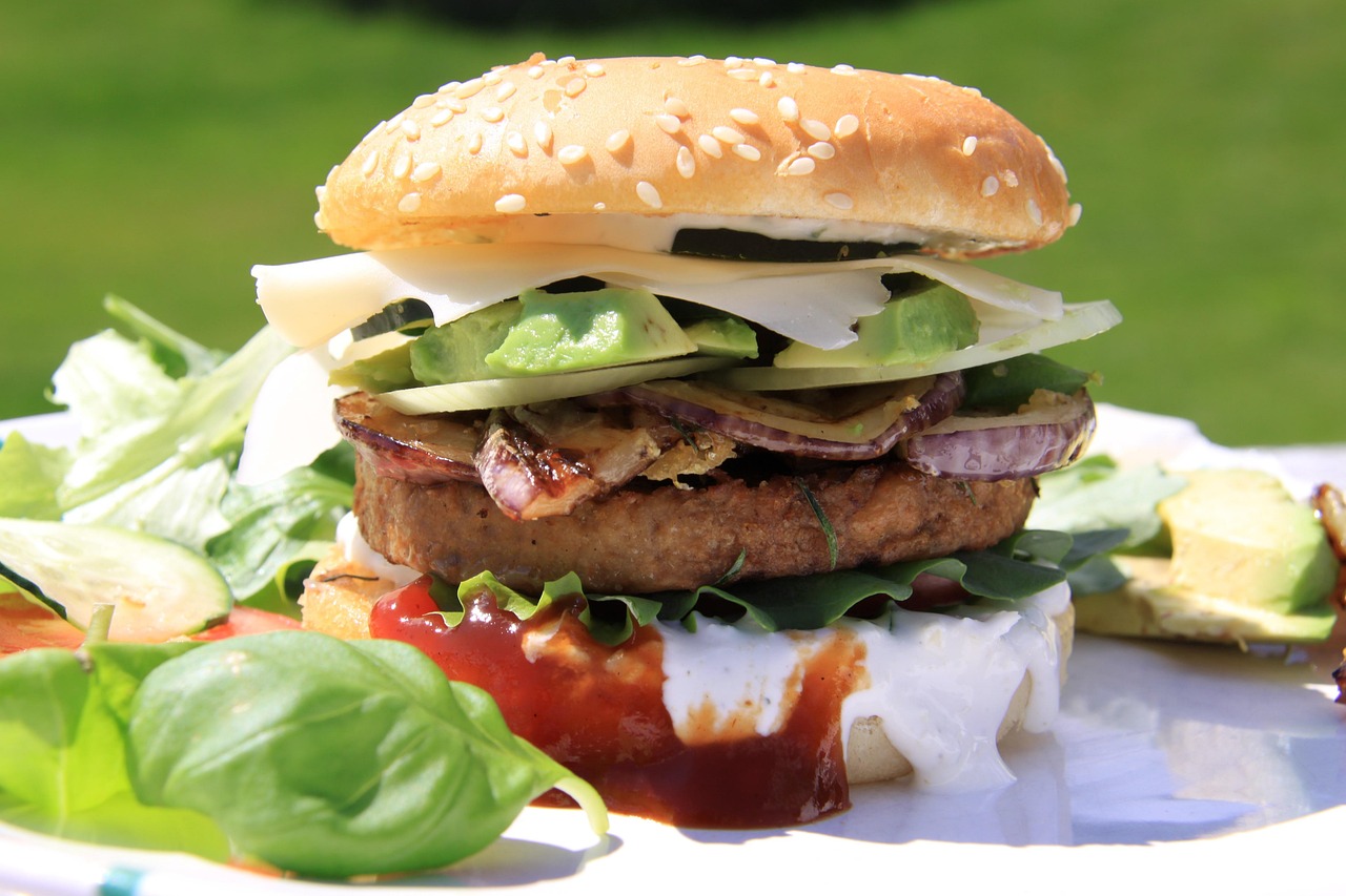 A delicious veggie burger on a bun with fresh avocado, tomato, onion, and lettuce on a wooden board