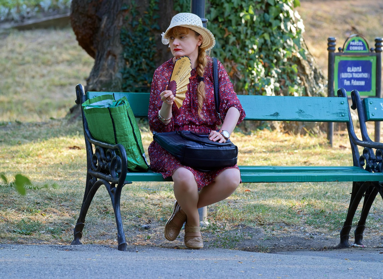 A woman relaxing on a park bench using a hand fan to stay cool during a summer heat wave, demonstrating natural cooling strategies without air conditioning