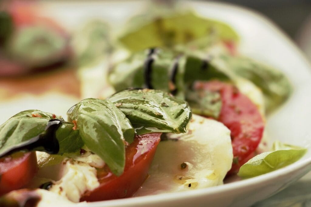 Fresh mozzarella cheese in a Caprese salad with sliced tomatoes, basil leaves, and balsamic glaze on a white plate - best mozzarella brand for healthy meals
