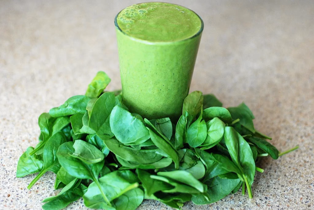 Vibrant green smoothie in a glass surrounded by fresh spinach leaves on a wooden surface, representing leafy greens for brain health and dementia prevention